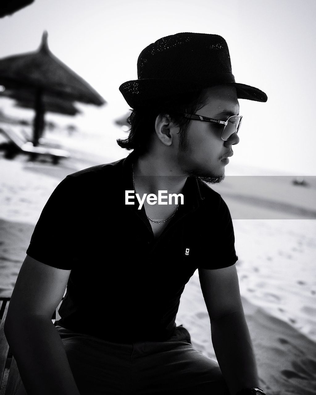 YOUNG MAN LOOKING AWAY WHILE SITTING ON SHORE