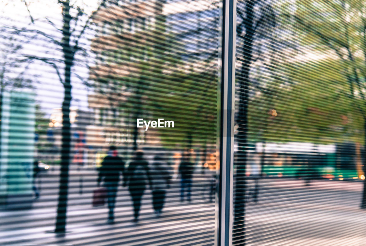 People walking on street seen through glass window in city