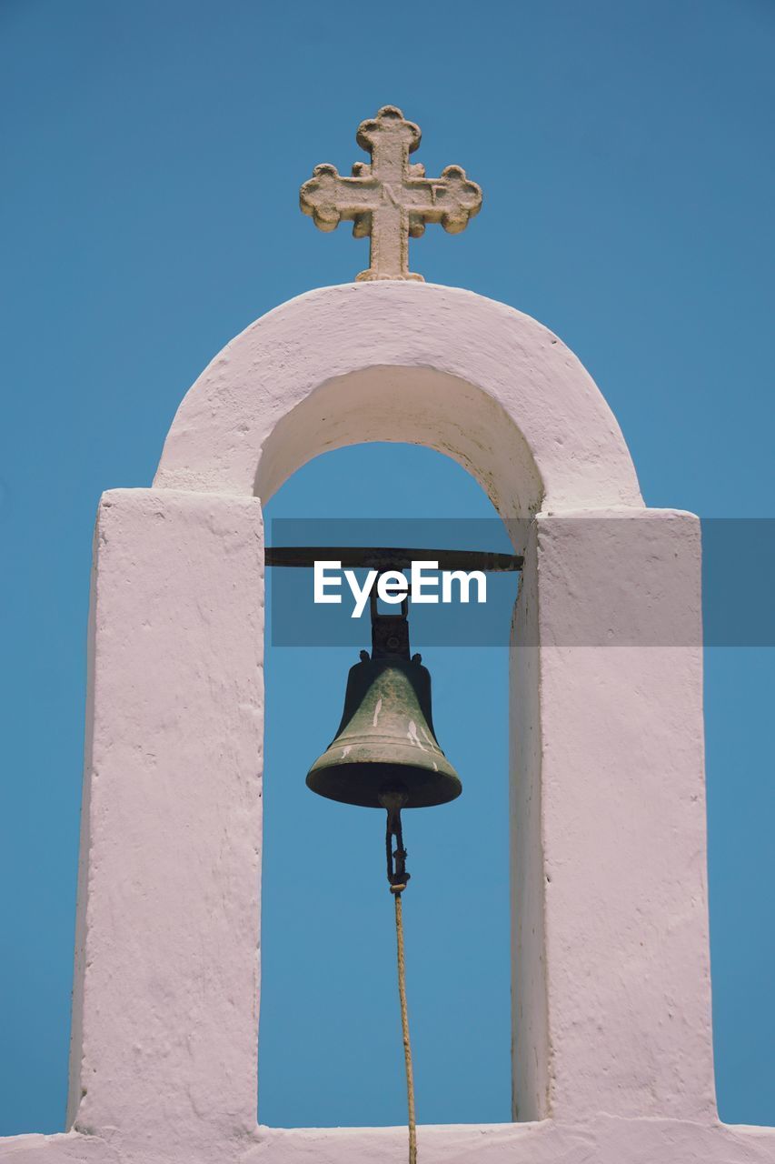 Low angle view of bell and white wall against blue sky