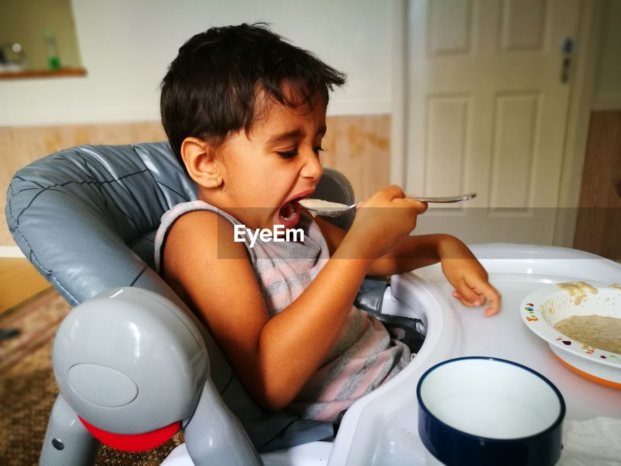 Boy eating food with spoon at home