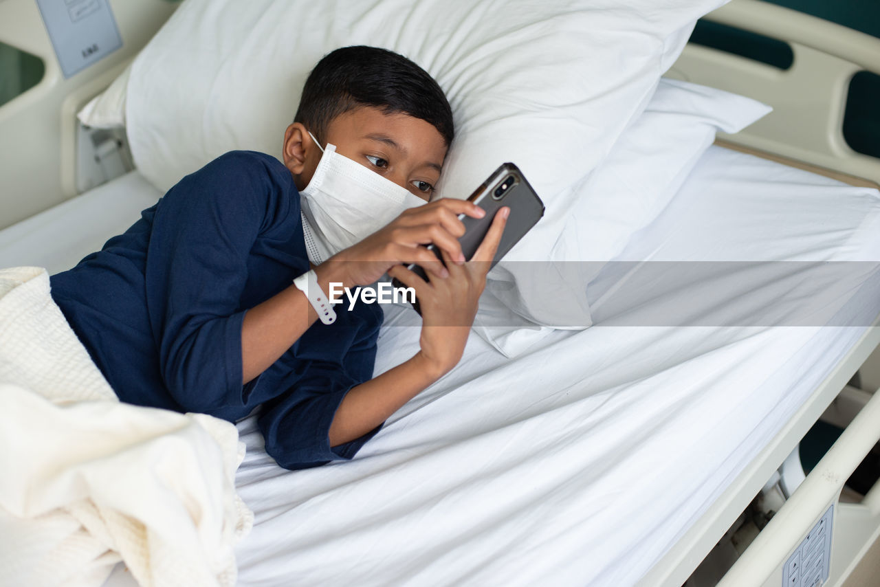 Boy wearing mask using mobile phone at hospital