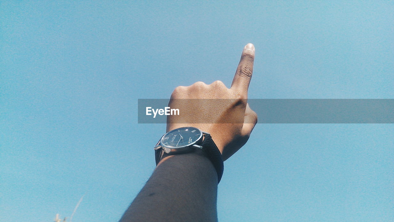 Cropped hand of person pointing towards clear sky