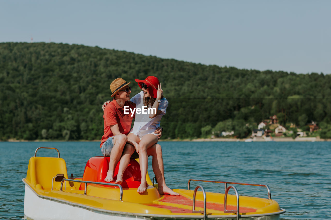 WOMAN SITTING ON BOAT AGAINST LAKE