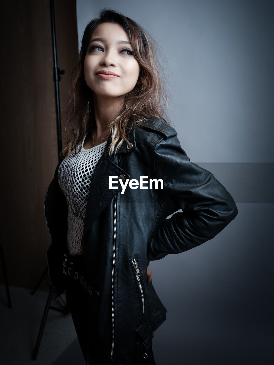 one person, portrait, women, adult, young adult, hairstyle, long hair, looking at camera, photo shoot, studio shot, indoors, leather, fashion, black, jacket, clothing, leather jacket, standing, arts culture and entertainment, brown hair, smiling, gray, waist up, female, three quarter length, textile, happiness, front view, gray background, casual clothing, person, emotion, glamour, lifestyles, individuality