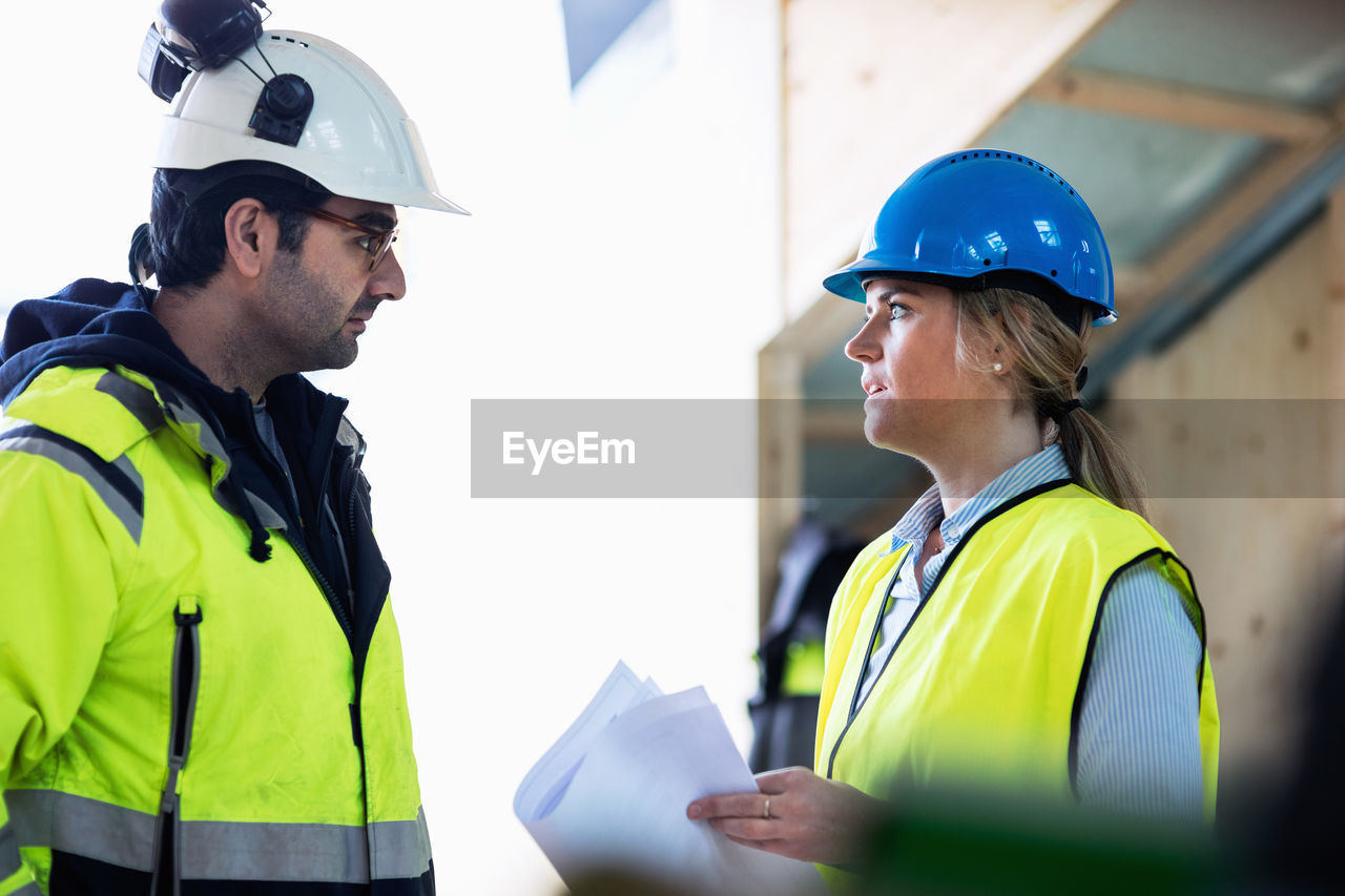 Male and female managers discussing over document at construction site