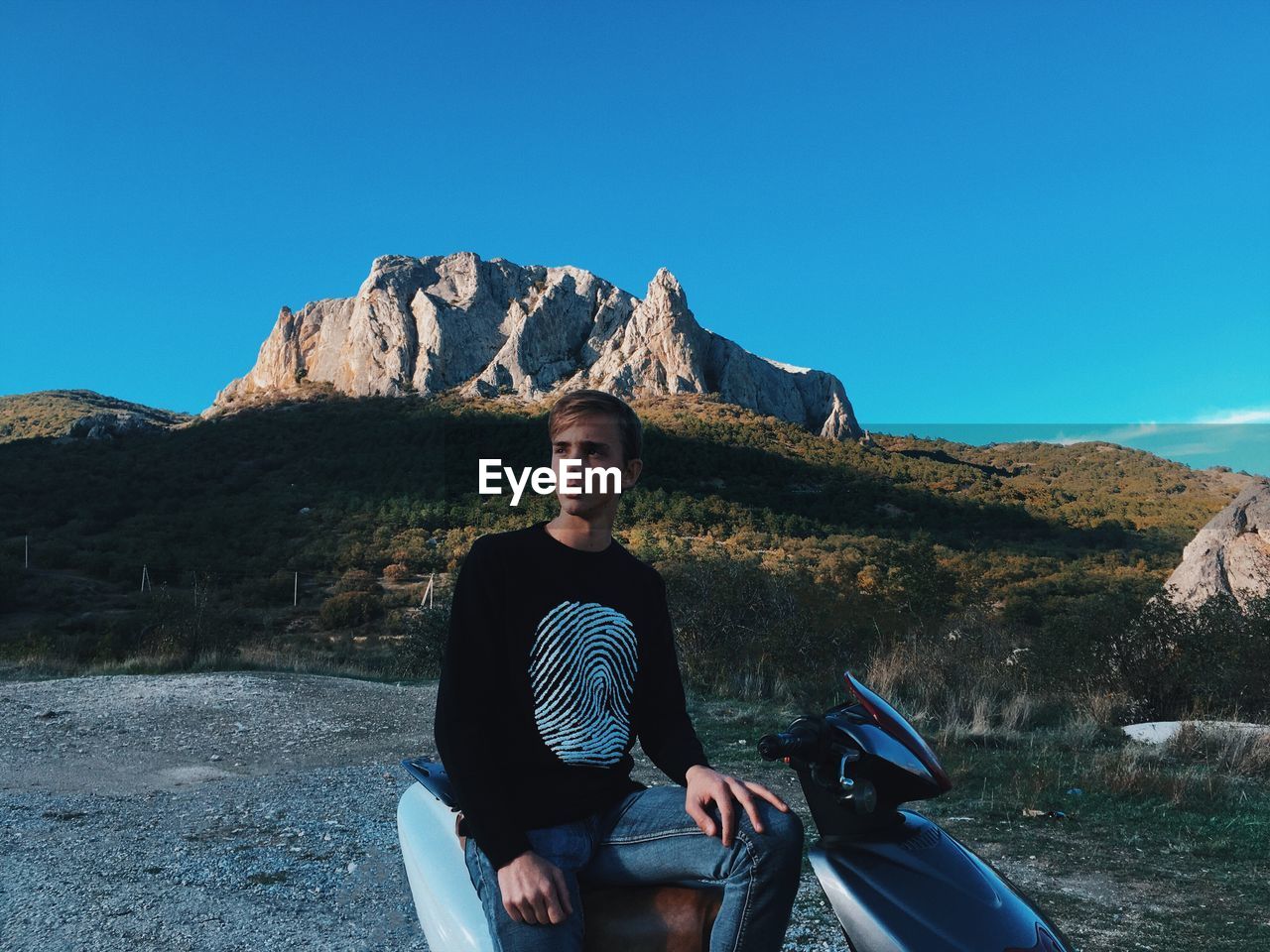 Man sitting on motorcycle against mountains