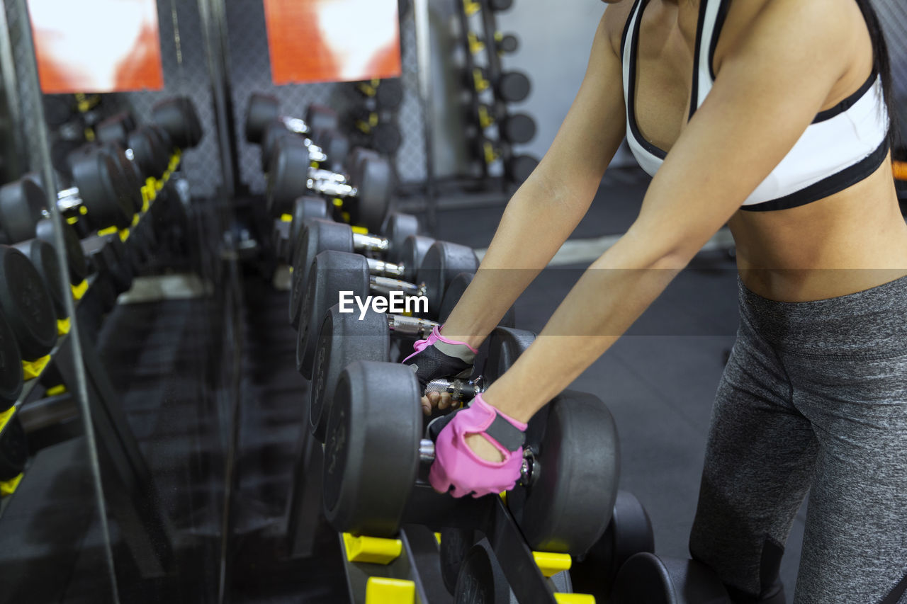 Midsection of woman lifting dumbbell at gym