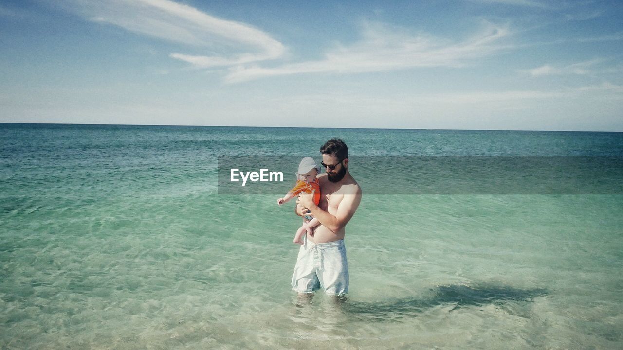 Man standing in sea with baby