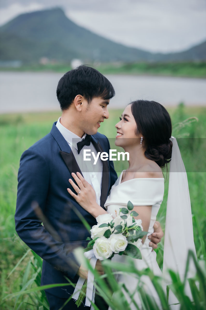 Couple holding bouquet standing against lake