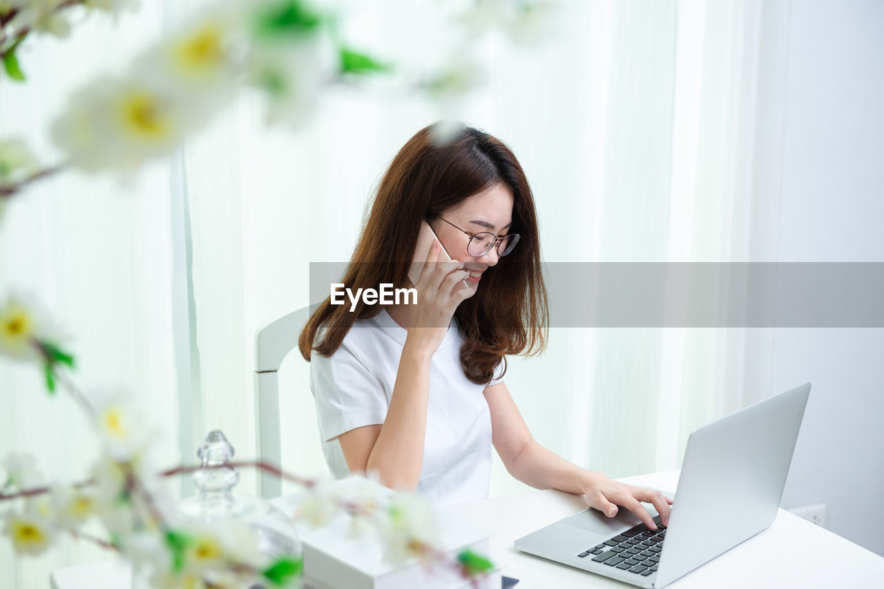 Woman talking on phone while using laptop at table