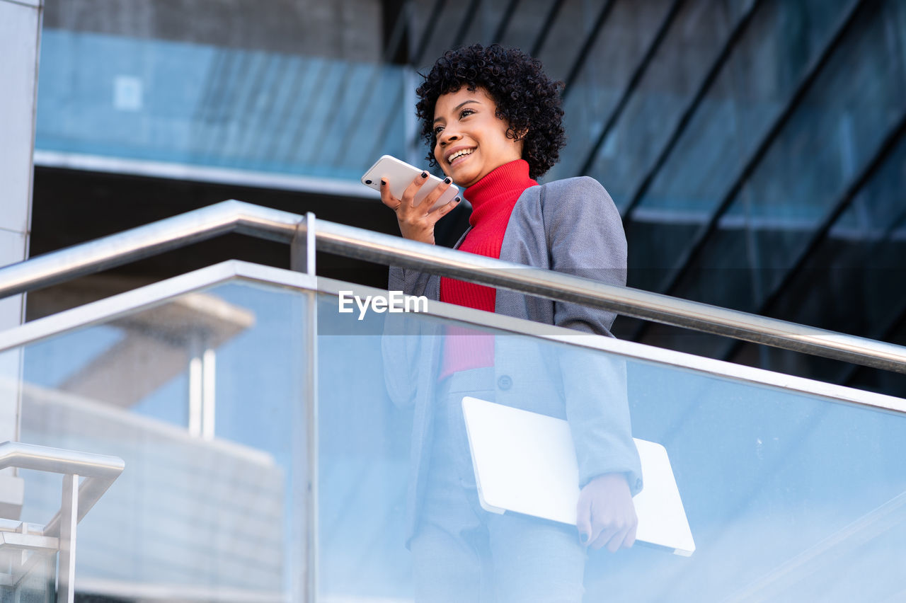 Young african american businesswoman in a suit in a corporate building holding the phone and laptop