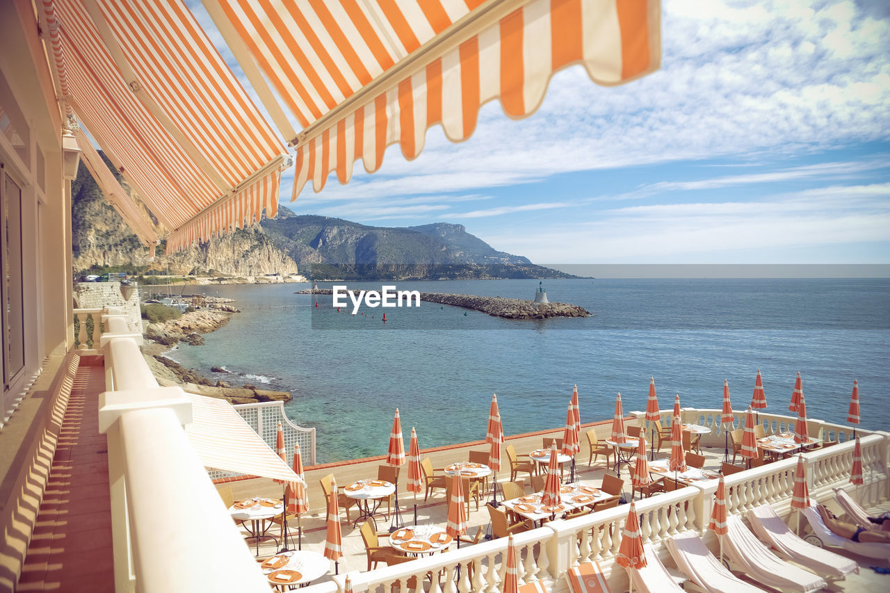 Tables and chairs with deck chairs in luxury hotel by sea against sky at monte carlo