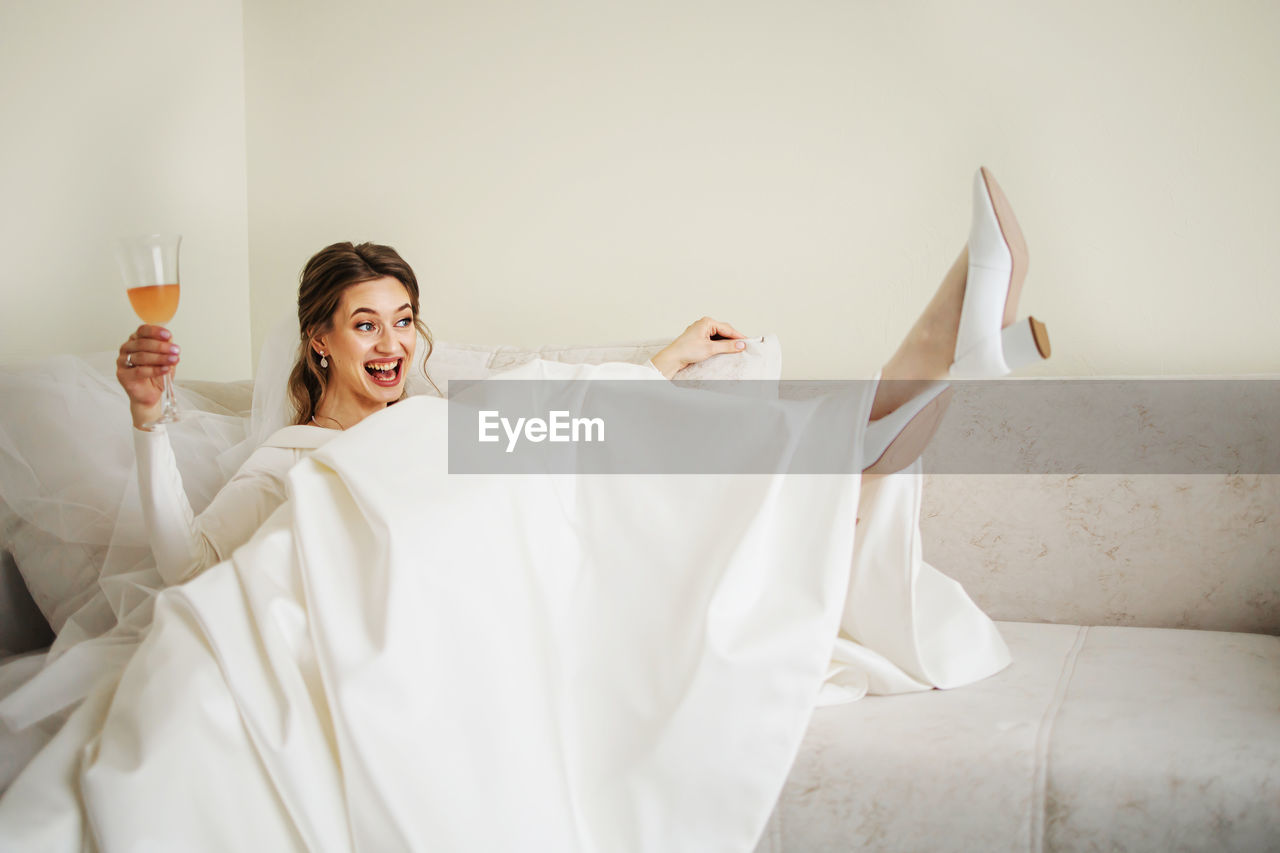 Happy bride holding champagne glass in bedroom