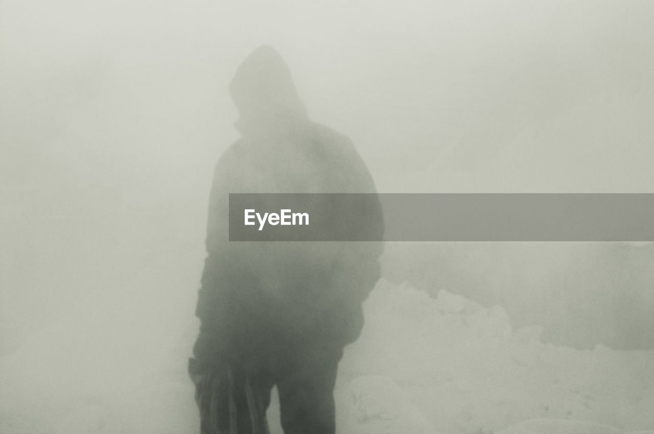 REAR VIEW OF MAN WALKING ON SNOW COVERED LANDSCAPE AGAINST SKY