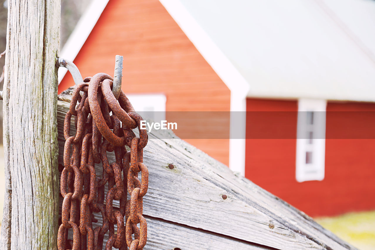 Close-up of rusty metal chains in front of fishing environments and against red wooden building