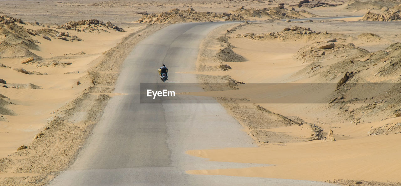 Rear view of man riding motorcycle on road at desert