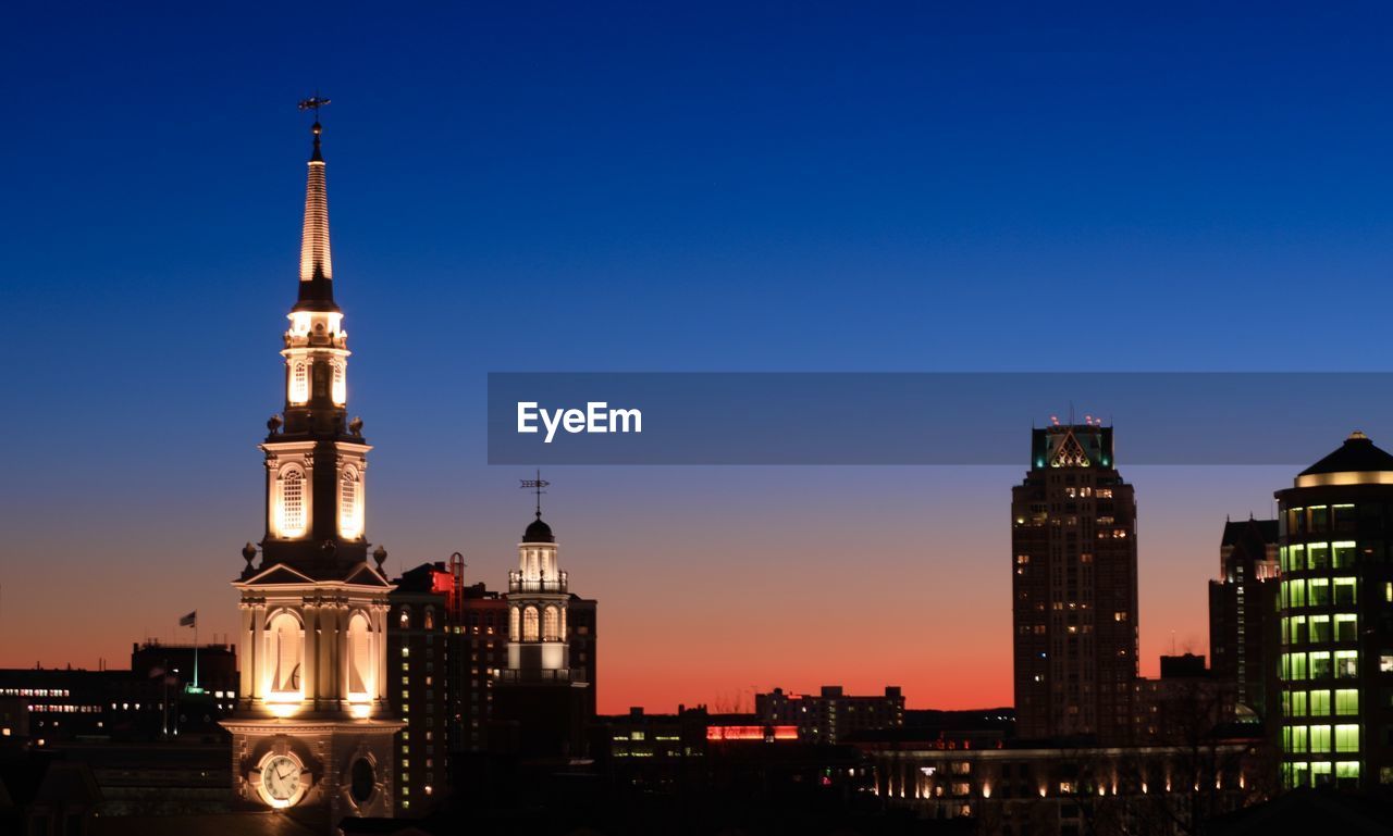 Illuminated buildings against clear sky at sunset