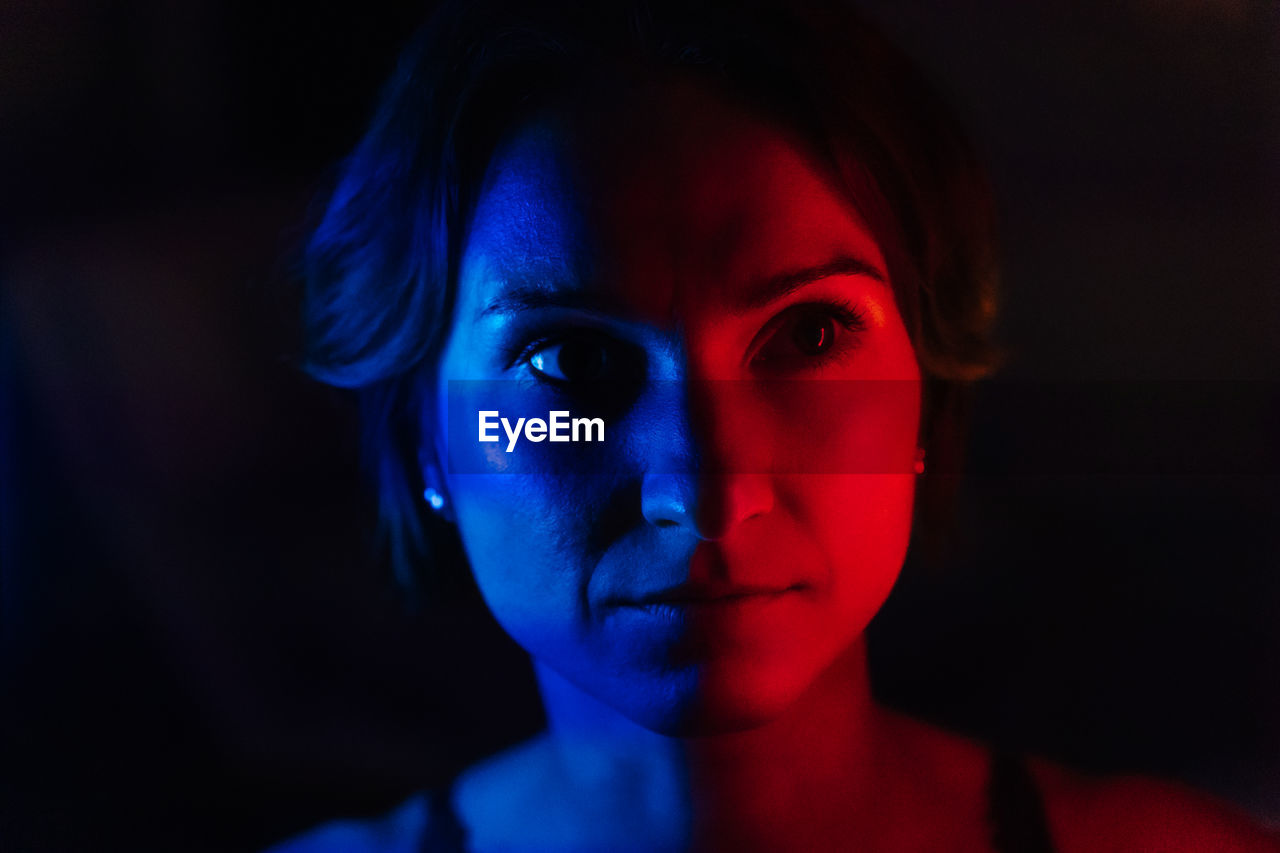 The face of a young woman in blue and red neon light on a dark background