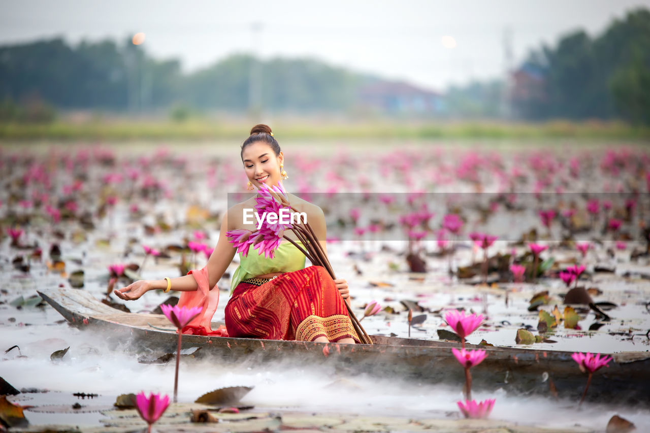 Smiling young woman holding water lilies in boat on lake