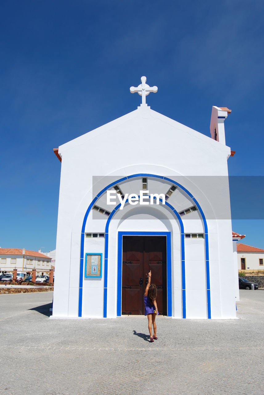 Girl pointing toward church against clear sky