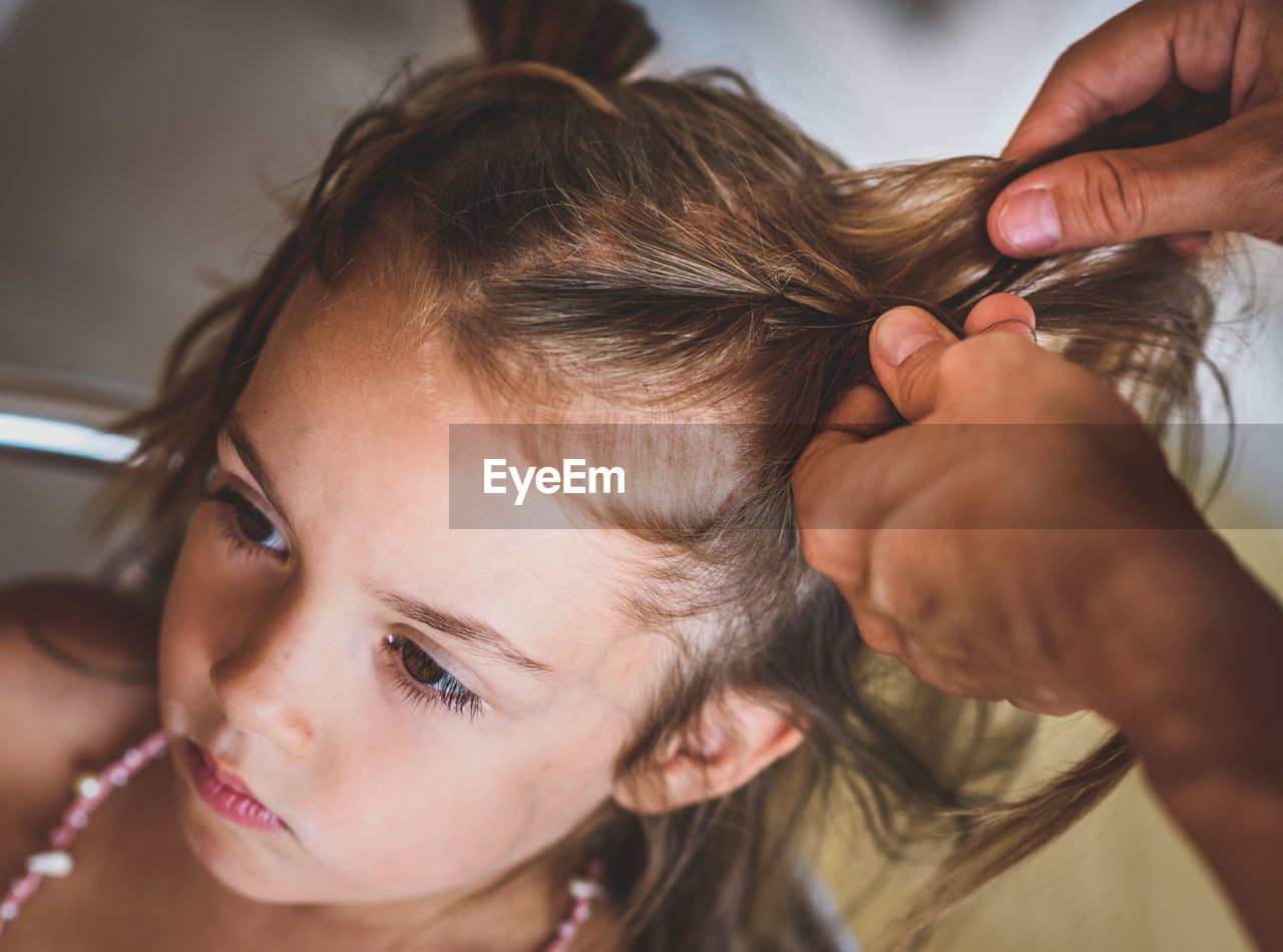 Cropped hands of mother braiding daughter hair