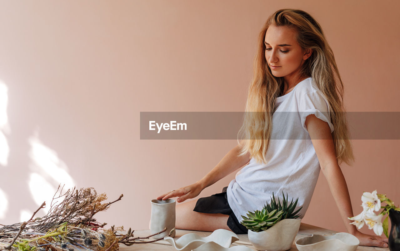 Side view of young woman sitting on table against wall