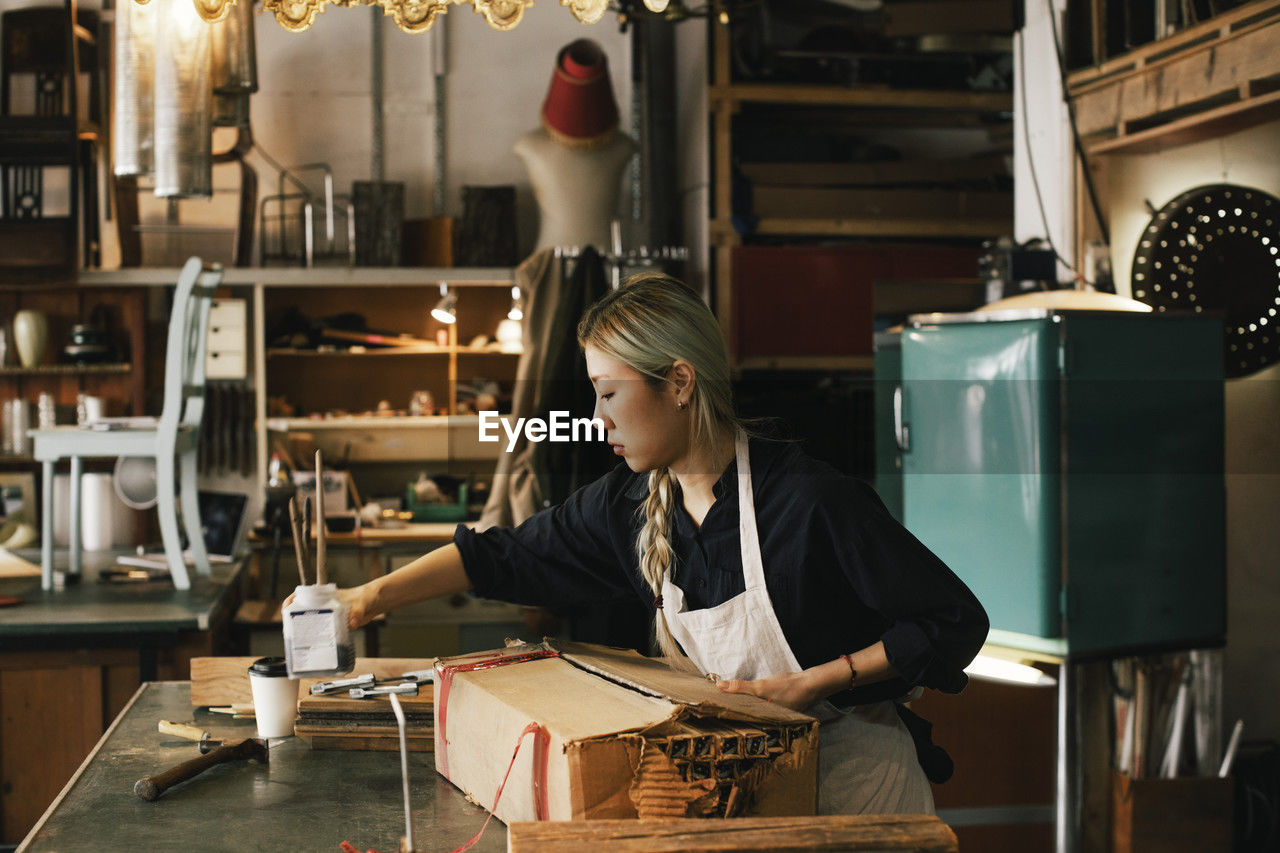 Young female entrepreneur working at workbench in workshop