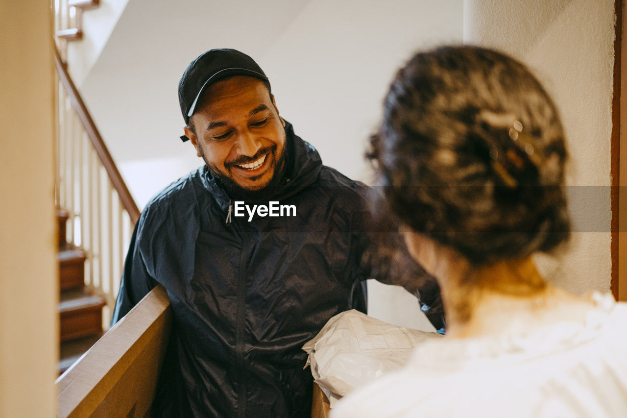 Smiling male delivery person delivering parcel to woman at doorway