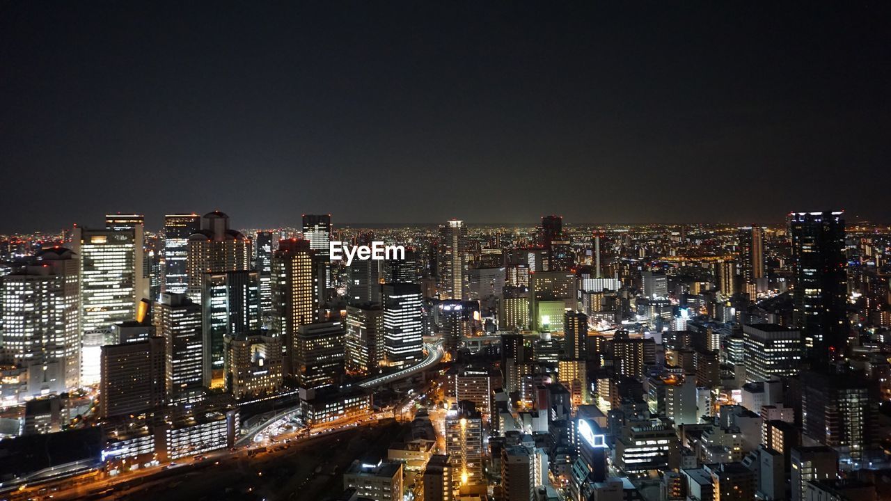 Illuminated modern buildings in city against sky at night