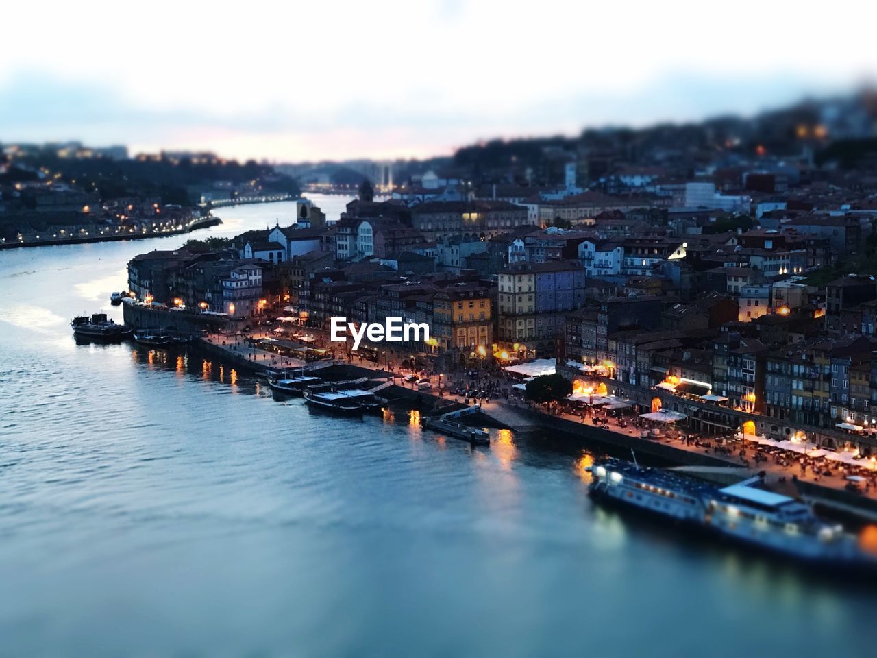 Illuminated buildings by river against sky in city