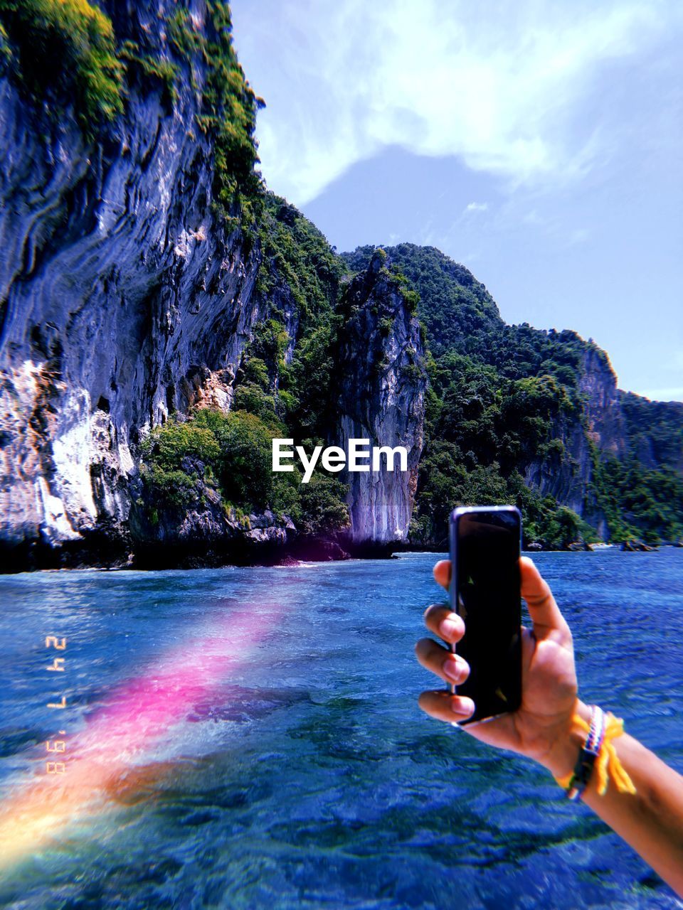 Cropped hand of person using mobile phone over lake against mountain