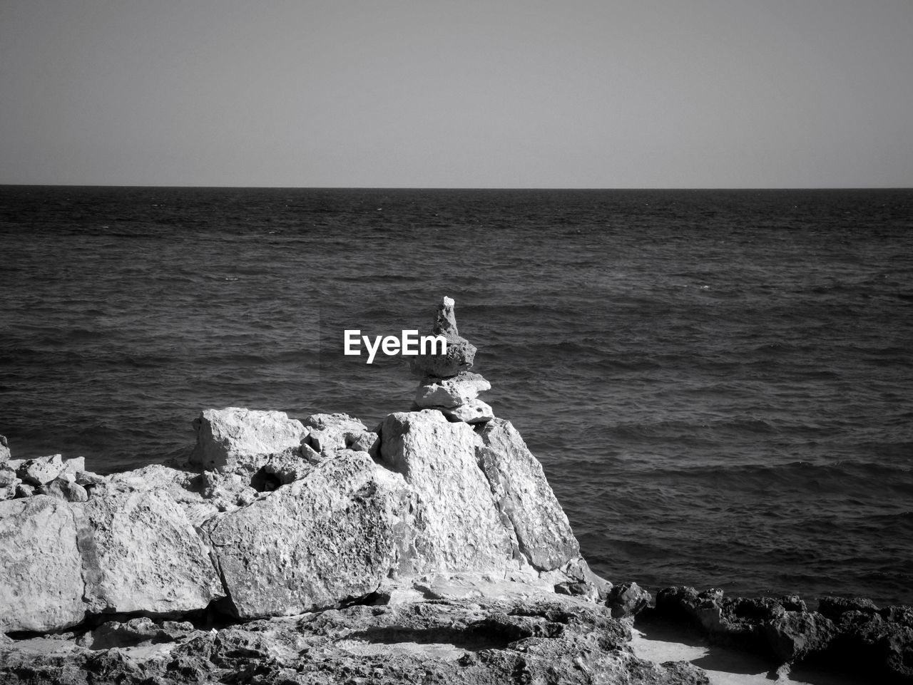 Sea in front of rock stack against clear sky