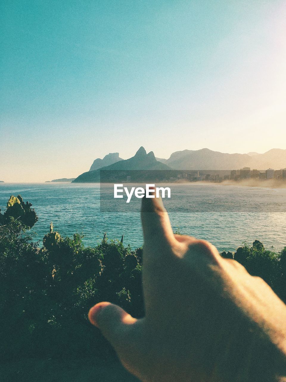 Cropped image of man pointing at mountain by sea against sky