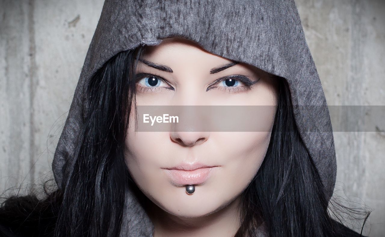 Close-up portrait of young woman wearing hooded shirt by wall