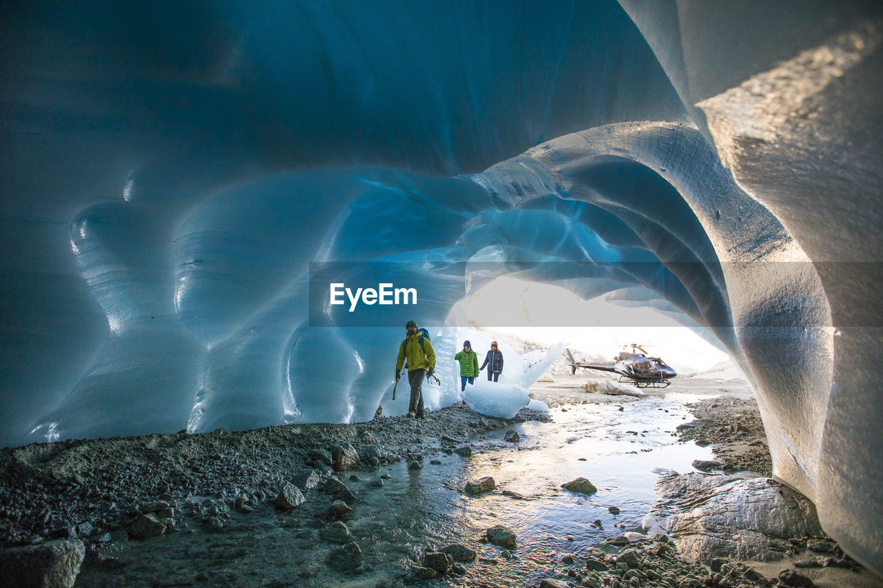 Three ice climbers enter a glacial cave.
