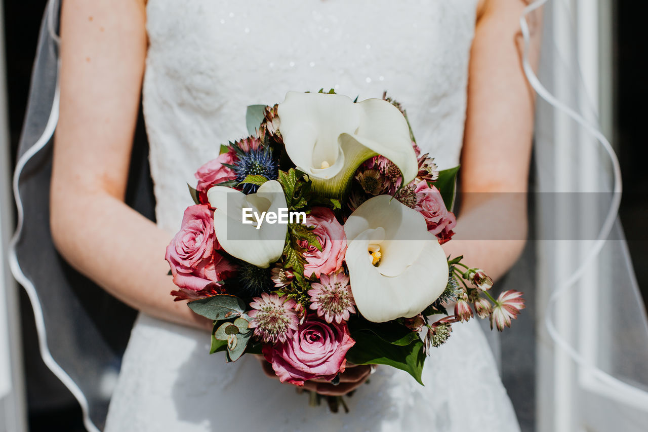 Midsection of bride holding bunch of flowers