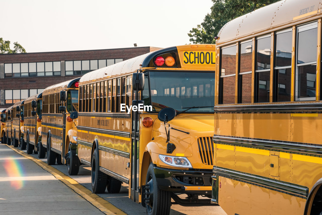 Yellow school buses lined up along sidewalk in front of school