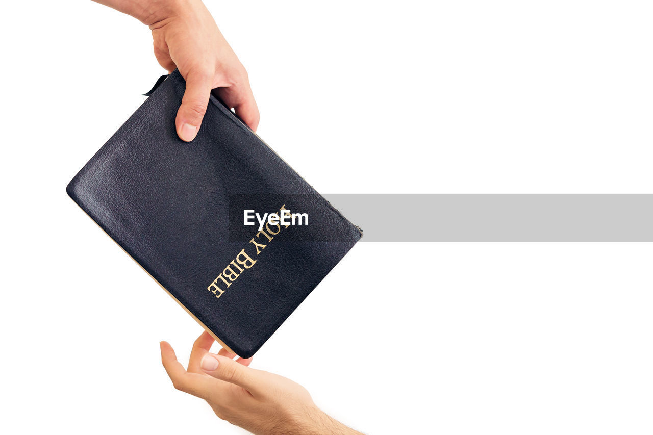 Cropped hand giving bible to person against white background