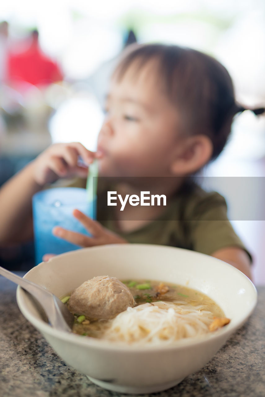Soup bowl on table with girl having drink in background at restaurant