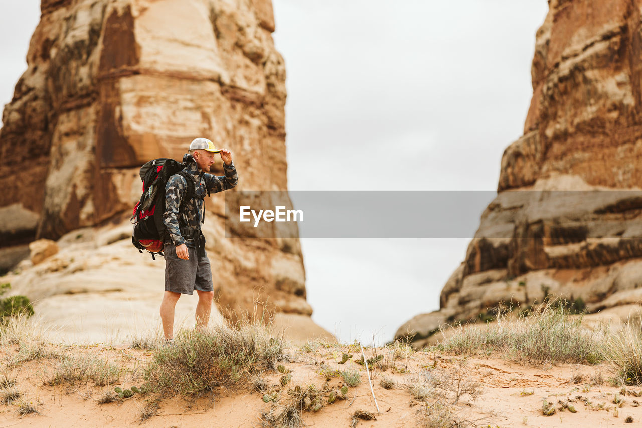 Hiker with big backpack pauses under red rock structures in utah