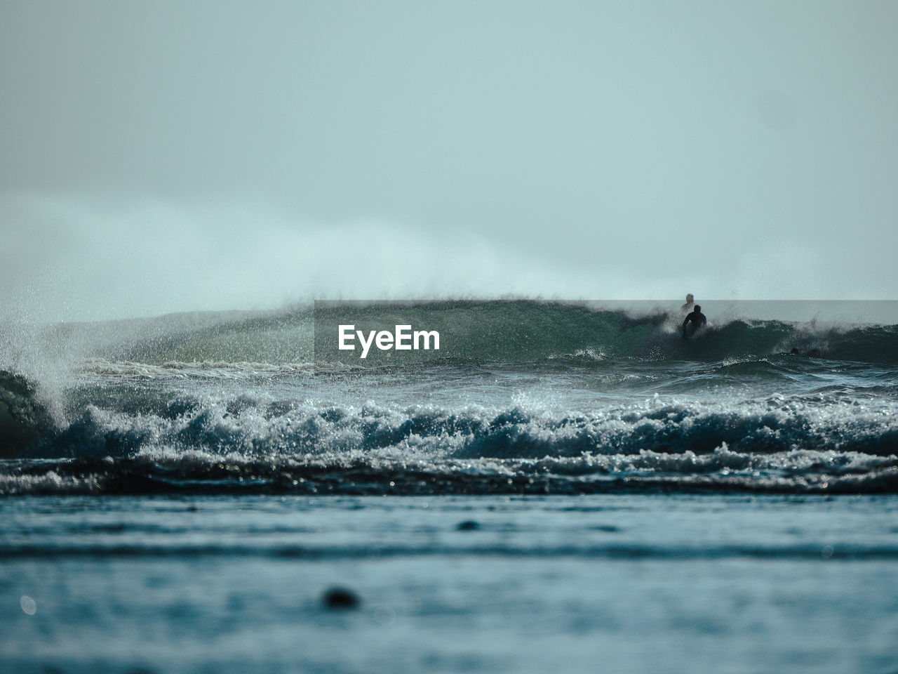 Scenic view of waves breaking in sea against cloudy sky