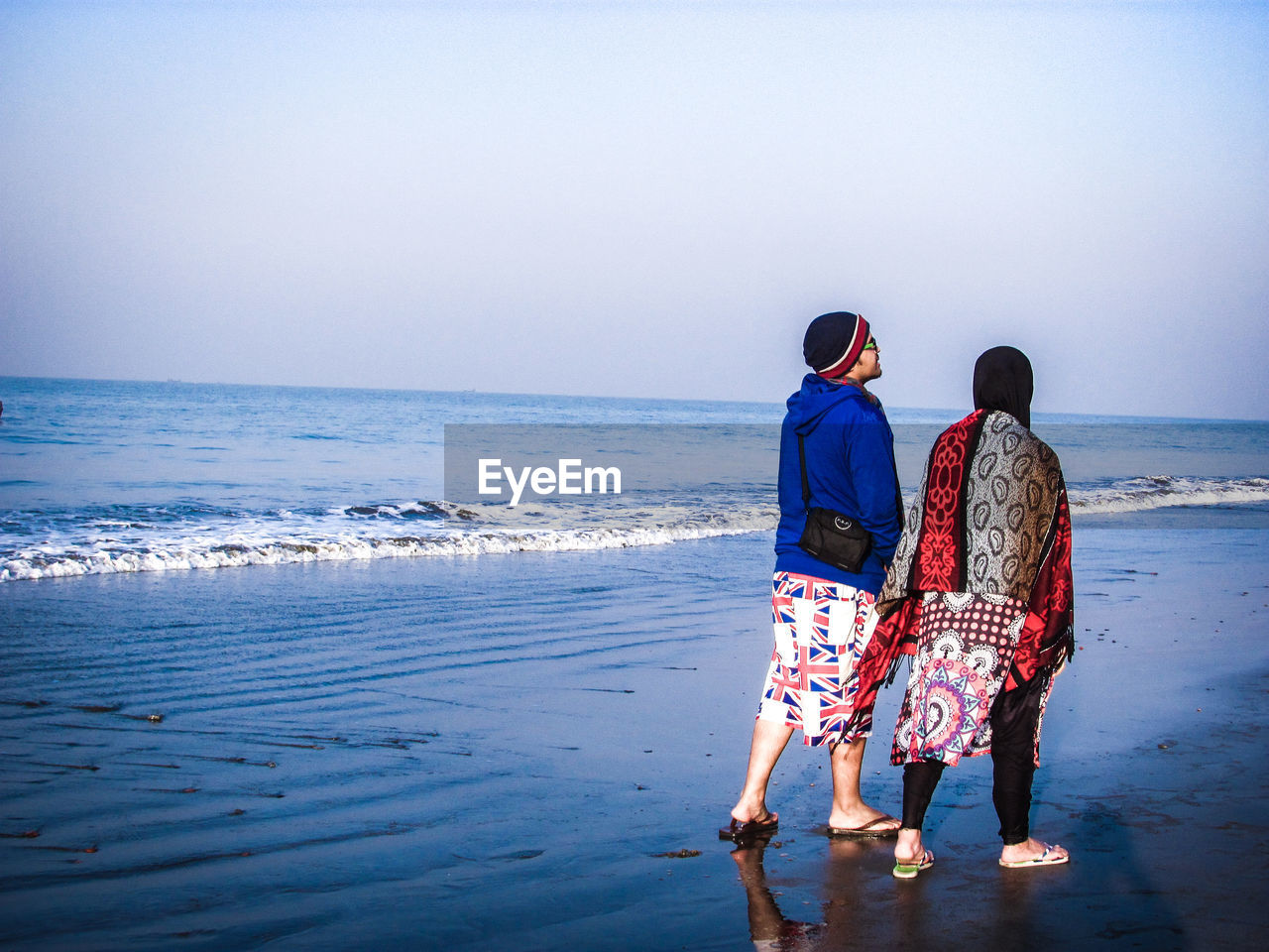 REAR VIEW OF FRIENDS STANDING AT BEACH AGAINST CLEAR SKY