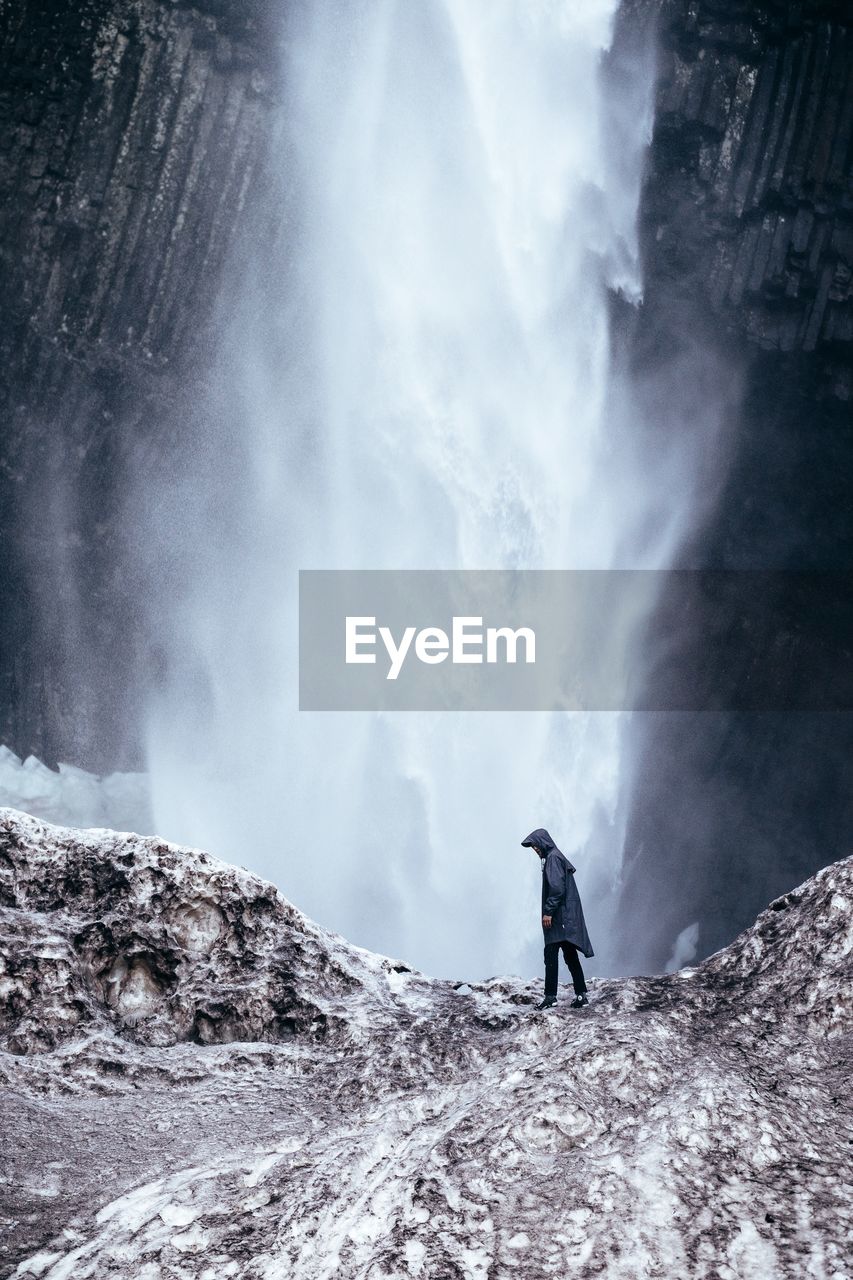 Man standing on rock by waterfall in forest