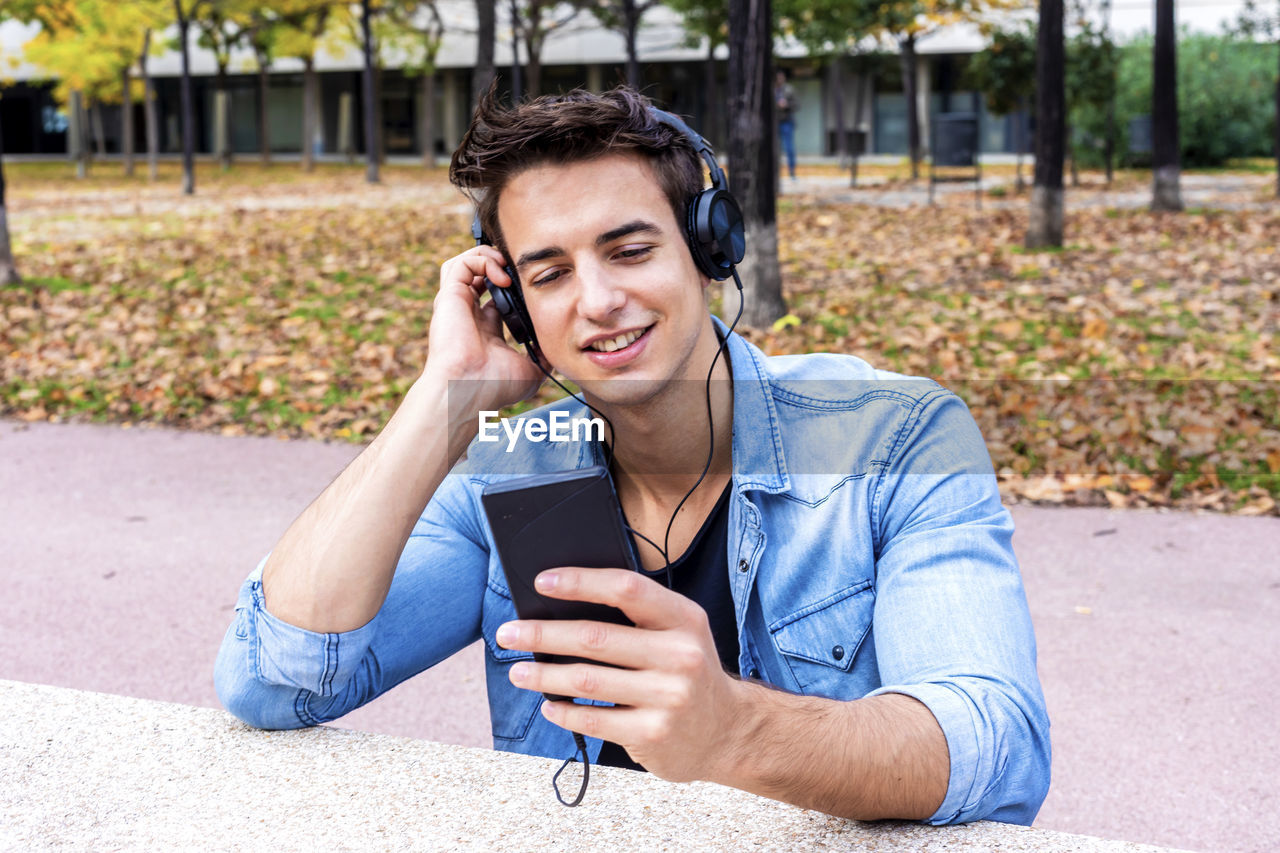 Man listening music while using mobile phone in city
