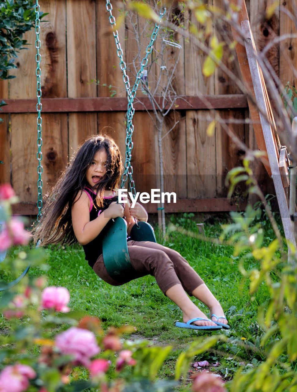 Girl playing on swing against fence at yard