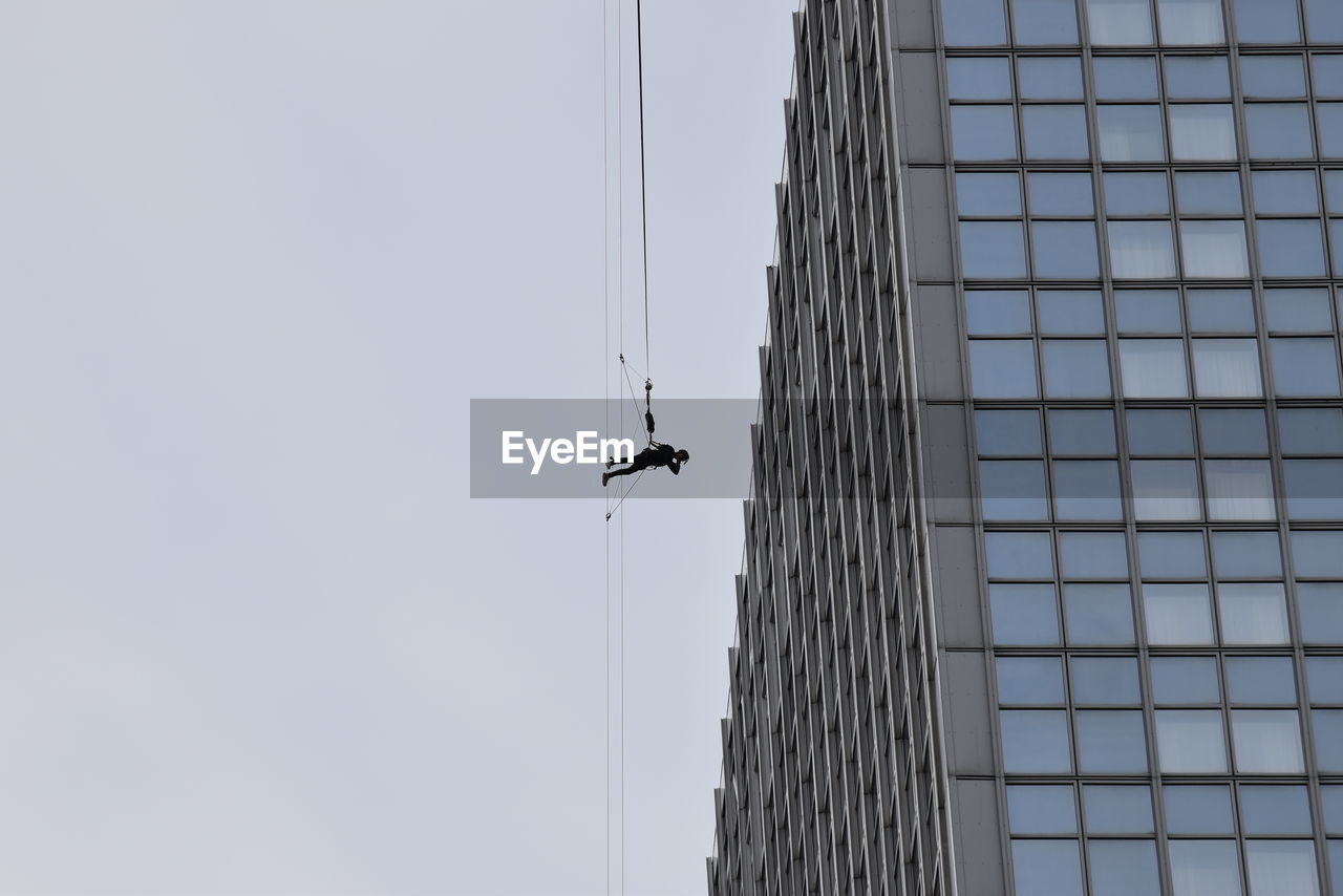 Low angle view of man hanging at crane against building