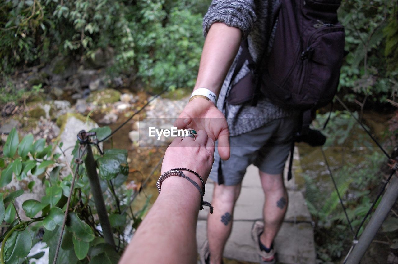 Cropped image of woman holding man hand on footpath