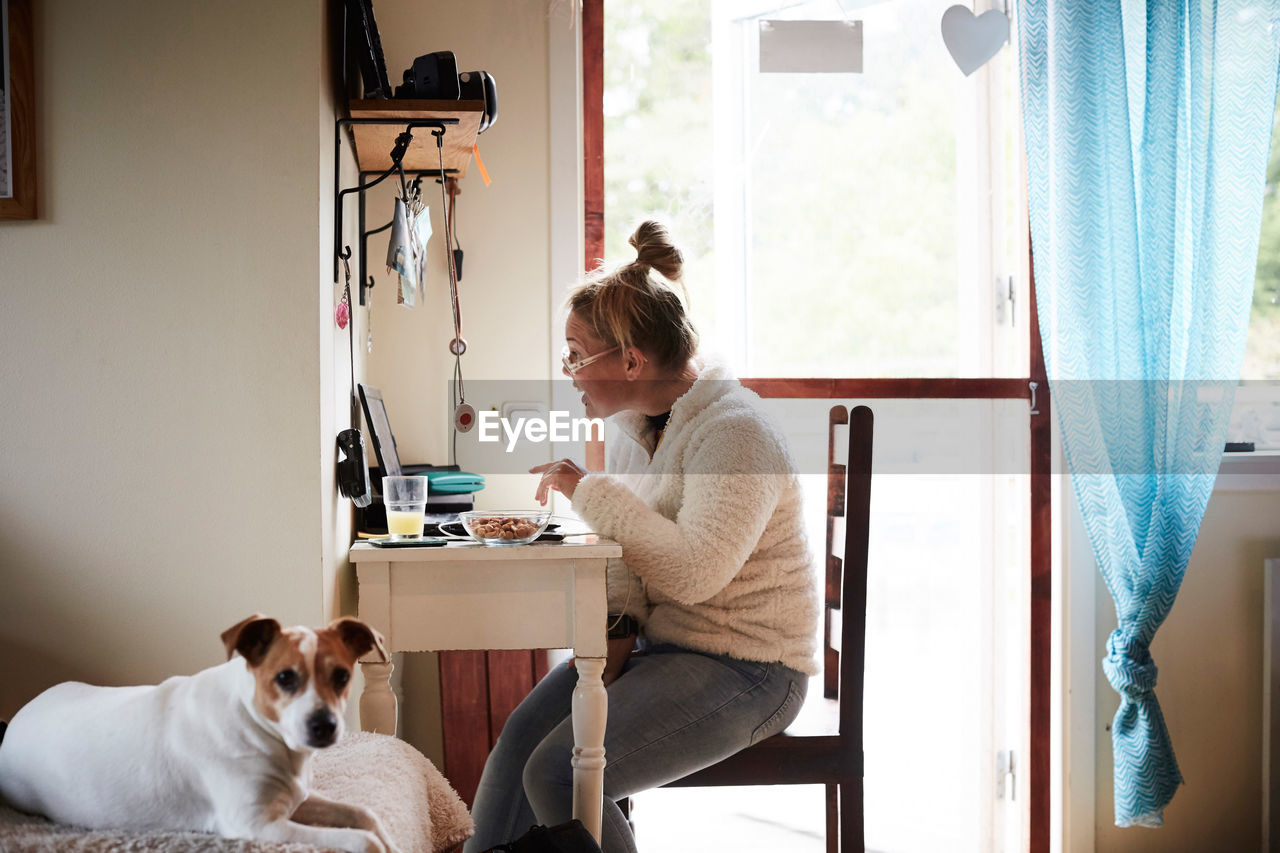 Disabled young woman using laptop at desk with dog in foreground at home