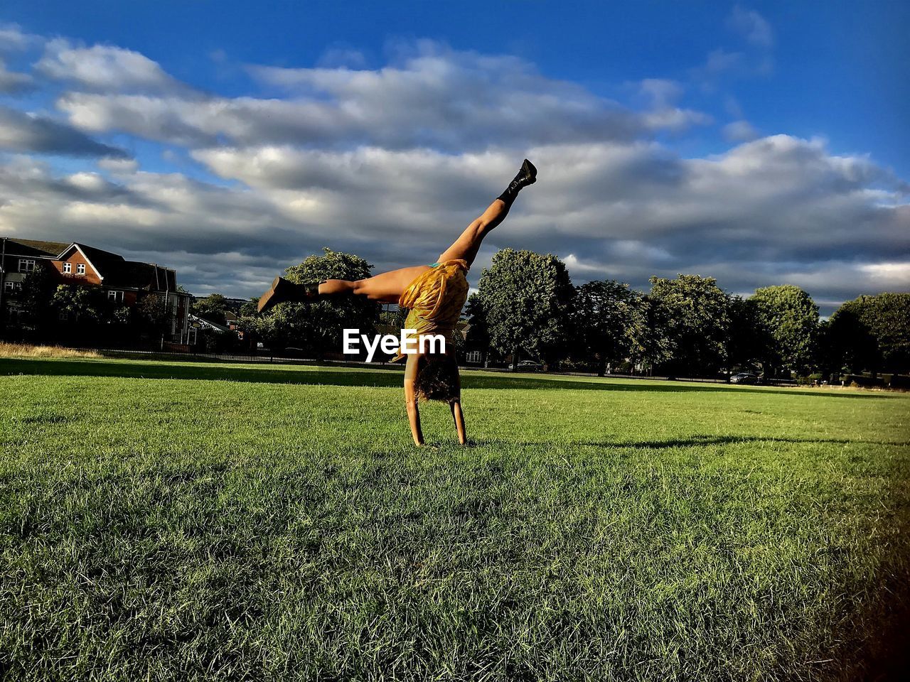 Woman practicing cartwheel at park against sky