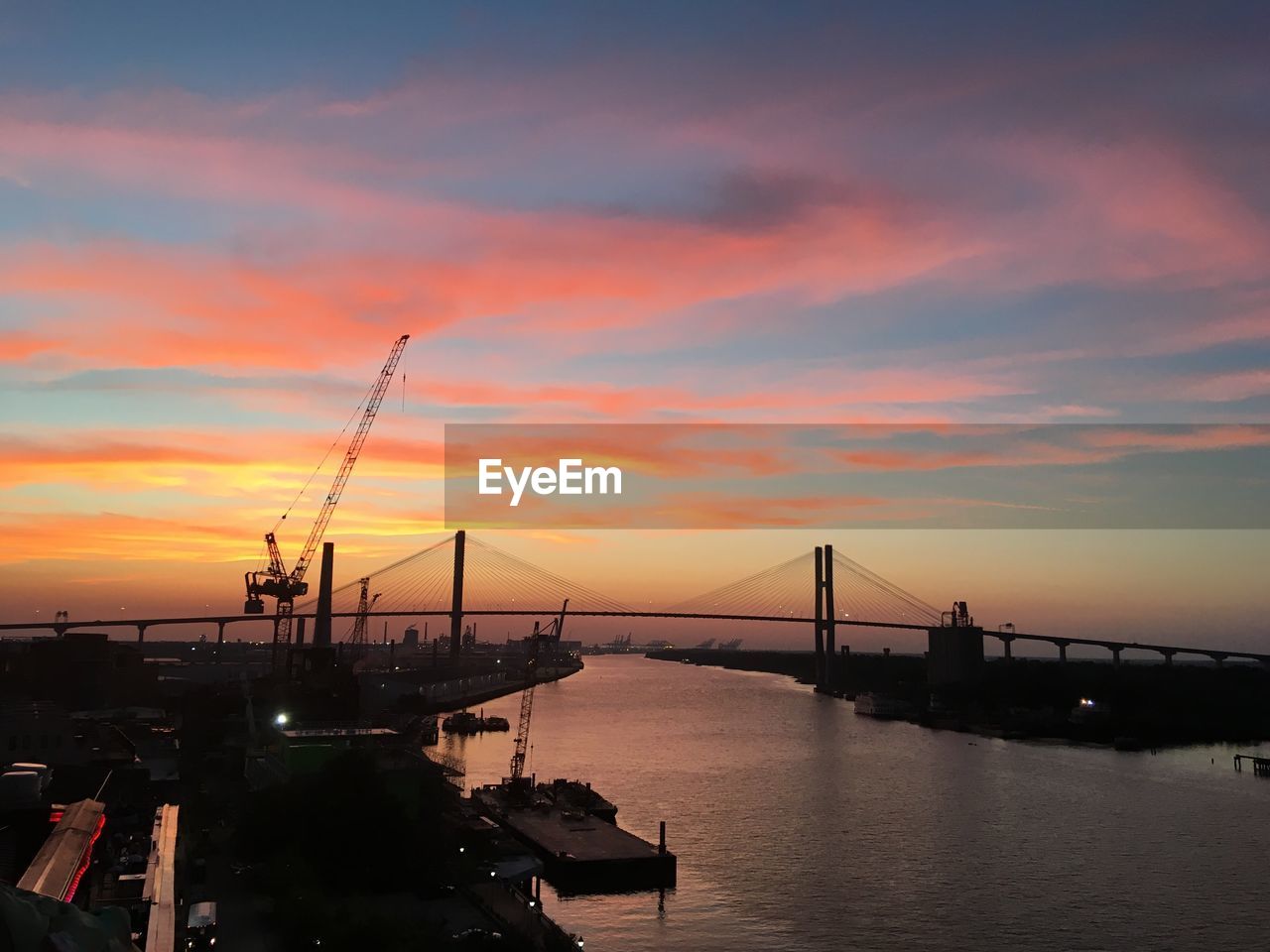 Silhouette bridge over river against sky during sunset